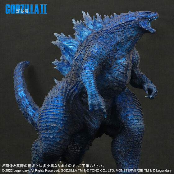 Một hình ảnh quảng cáo cho "Dòng Gigantic Godzilla (2019) Blue Clear Ver." hình từ Premium Bandai với hình ảnh một nửa của đồ chơi từ một bên.